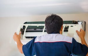 Technician carefully disassembling an aircon unit for chemical washing, revealing grime build-up.